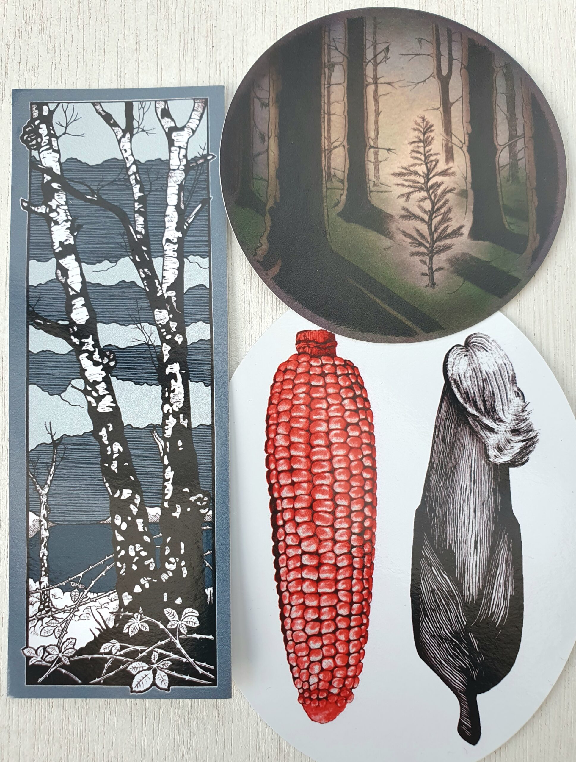 Image shows three stickers with hand drawn illustrations from issue four: one with a cob of red maize next to a sheathed cob with cornfield; one of the little fir tree in the forest amongst tall trees; and one with the front cover image of birches and chaga.