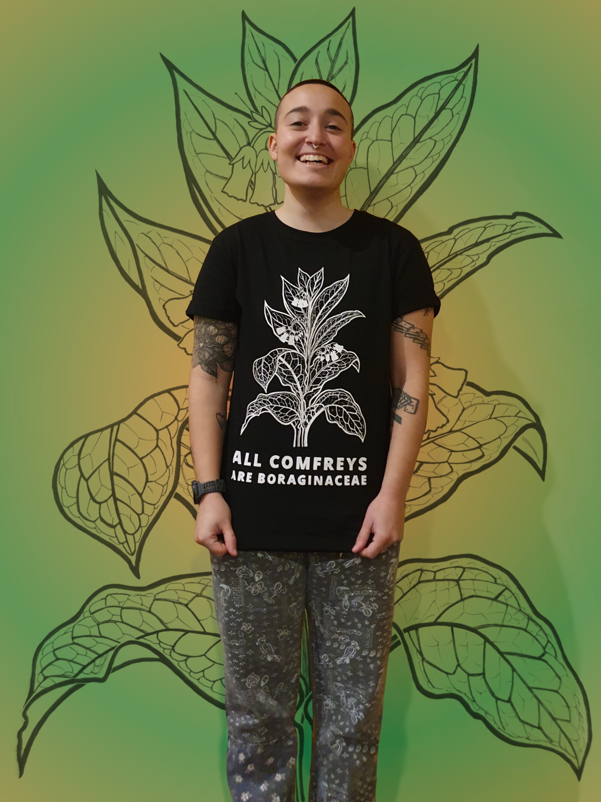 A black cotton t shirt with illustrated comfrey design and hand lettering with the words 'all comfreys are boragniaceae'
